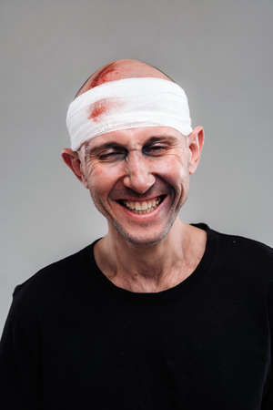 Against a gray background stands a battered and battered man in a black T-shirt with his head wrapped in a bandage.の写真素材