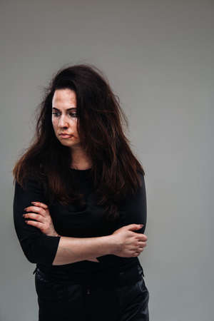 a battered woman in black clothes on an isolated gray background. Violence against women.の写真素材