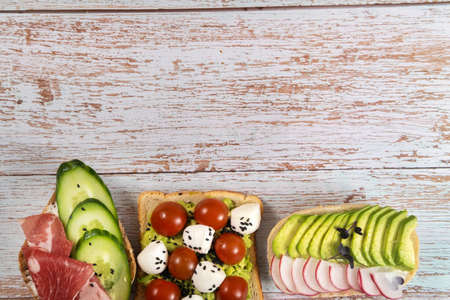 An assortment of sandwiches with fish, cheese, meat and vegetables lay on the wooden table.の写真素材