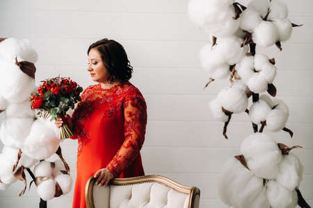 a woman in a red dress stands and holds a bouquet of red roses and strawberries in the interiorの写真素材