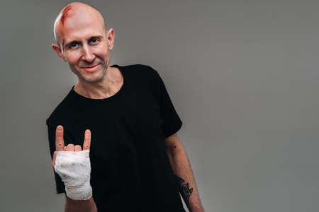 On a gray background stands a battered man in a black T-shirt With his hands wrapped up.