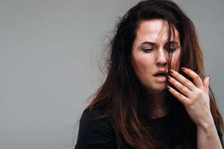 a battered woman in black clothes on an isolated gray background. Violence against women.の写真素材