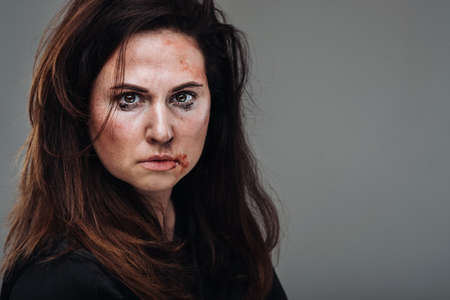 a battered woman in black clothes on an isolated gray background. Violence against women.の写真素材