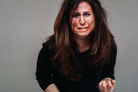 a battered woman in black clothes on an isolated gray background. Violence against women.の写真素材