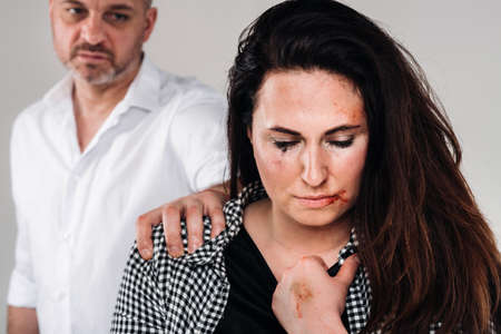 A woman beaten by her husband standing behind her and looking at her aggressively. Domestic violence.の写真素材
