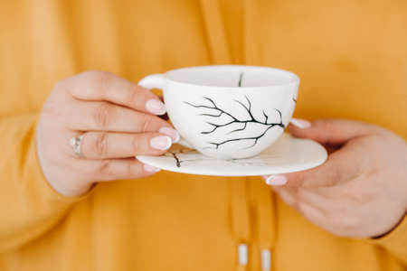 close up of the hands of a woman in an orange sweatshirt holding a coffee mug.の写真素材