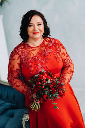 a woman in a red dress sits on a sofa and holds a bouquet of red roses and strawberries in the interiorの写真素材