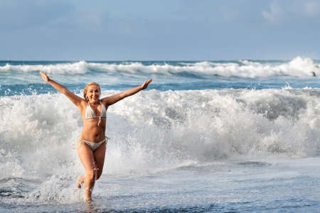 A girl with wet hair jumps over large waves in the Atlantic ocean, around a wave with splashes of spray and water drops. Tenerife.Spain.の写真素材