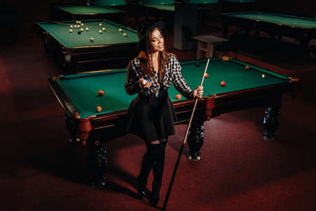 A girl in a hat in a billiard club with a cue in her hands.Pool Game.