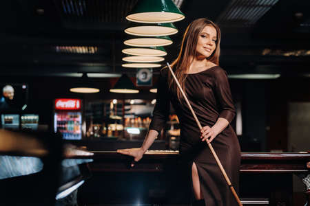 A girl in a hat in a billiard club with a cue in her hands.Pool Game.の写真素材