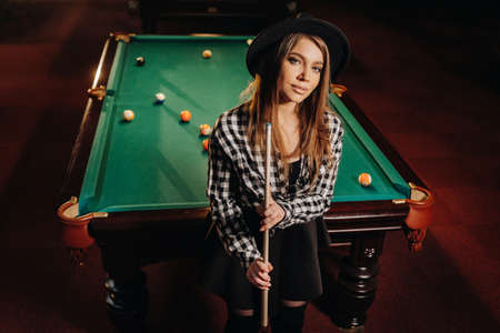 A girl in a hat in a billiard club with a cue in her hands.Pool Game.