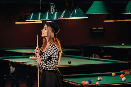 A girl in a hat in a billiard club with a cue in her hands.Pool Game.