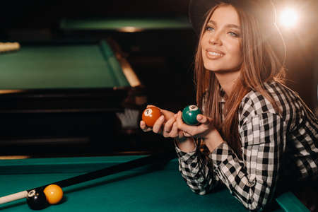 A girl in a hat in a billiard club with balls in her hands.Playing pool.の写真素材