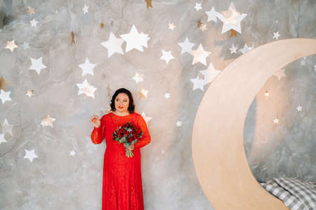 a woman in a red dress stands and holds a bouquet of red roses and strawberries in a fabulous studio.の写真素材