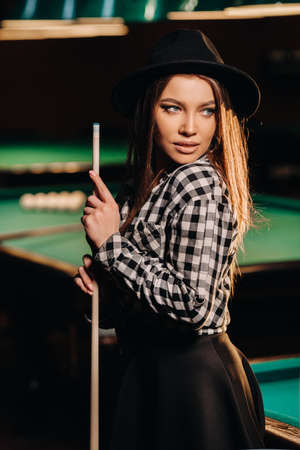 A girl in a hat in a billiard club with a cue in her hands.Pool Game.の写真素材