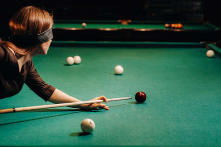A girl with a blindfold and a cue in her hands in a billiard club. Russian billiards.の写真素材
