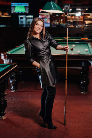 A girl with a cue in her hands is standing in a billiard club. Russian billiards.