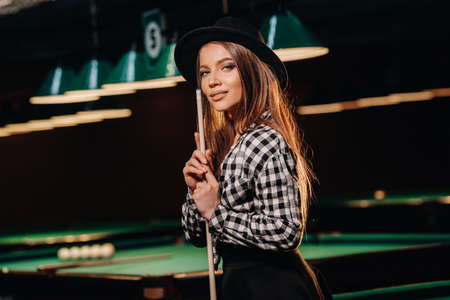A girl in a hat in a billiard club with a cue in her hands.billiards Game.の写真素材