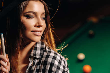 A girl in a hat in a billiard club with a cue in her hands.billiards Gameの写真素材