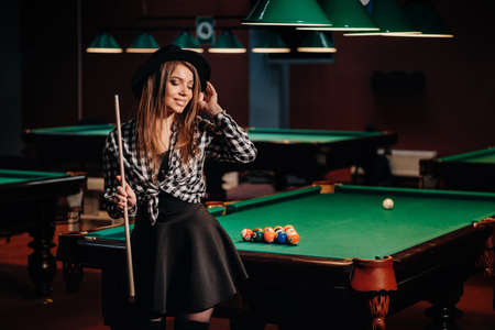 A girl in a hat in a billiard club with a cue in her hands.billiards Game.
