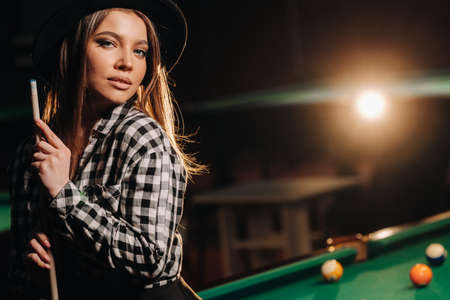 A girl in a hat in a billiard club with a cue in her hands.billiards Game.の写真素材