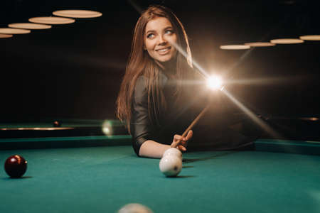 A girl with a cue in her hands makes a shot at a ball in a billiard club. Russian billiards.