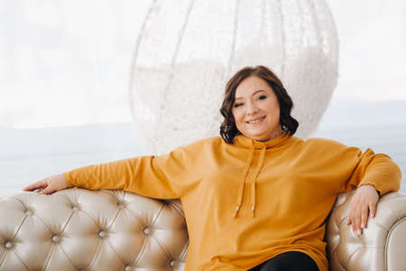 a woman in an orange hoodie sits on a white sofa.