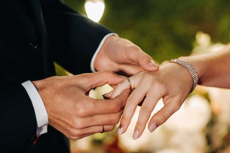 The groom puts an engagement ring on the bride's finger on their wedding day.の写真素材