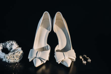 white wedding shoes and garter belt with earrings on a black background.の写真素材