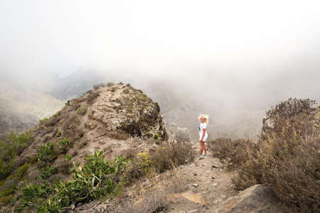 a girl in white clothes climbs to the top of a cliff on the island of Tenerife, Spainの写真素材