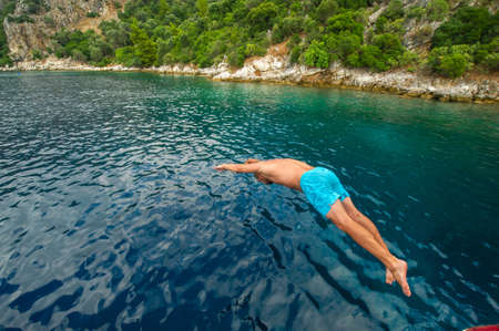 A man in blue shorts dives from a ship into the sea near the shore.