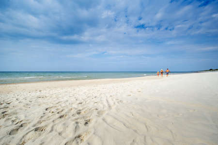 A little girl and her parents walk on the beach in swimsuits on the Baltic Sea in Lithuania.の写真素材