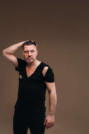 Against a gray background stands a battered angry man in a black T-shirt with wounds.の写真素材