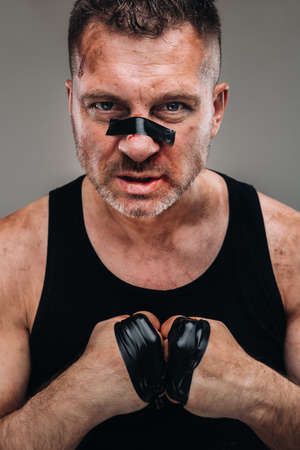 on a gray background stands a battered man in a black T shirt looking like a fighter and preparing for a fight.の写真素材