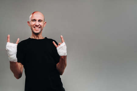 a battered man with his hands wrapped in a black T-shirt on a gray background, looking like a drug addict and a drunk.の写真素材