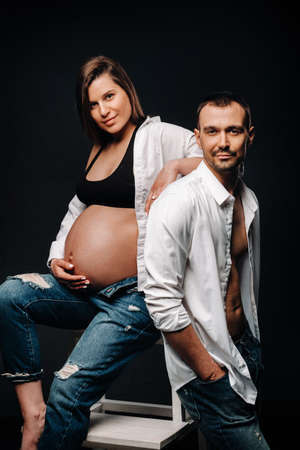 a pregnant woman and a man in a white shirt and jeans in a studio on a black background.の写真素材