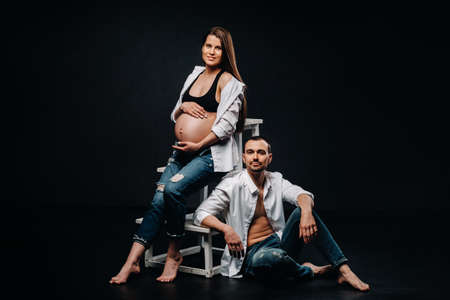 a pregnant woman and a man in a white shirt and jeans in a studio on a black background.の写真素材