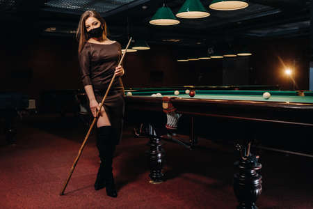 Masked girl in a pool club with a cue in her handsの写真素材