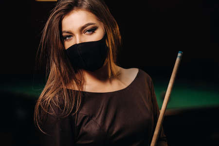 Masked girl in a pool club with a cue in her handsの写真素材