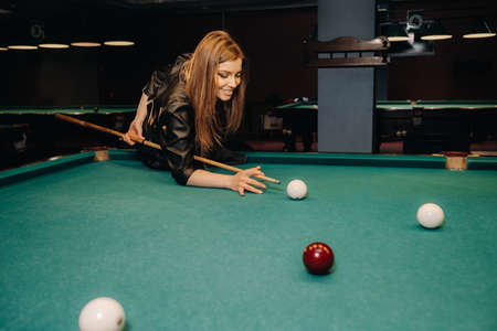 A girl with a cue in her hands makes a shot at a ball in a billiard club.Russian billiardsの写真素材