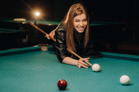 A girl with a cue in her hands makes a shot at a ball in a billiard club.Russian billiardsの写真素材