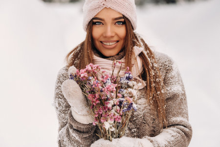 A girl in a sweater in winter with a bouquet in her hands stands among large snowdriftsの写真素材