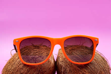 Two whole coconuts and orange glasses on a pink background.