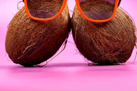 Two whole coconuts and orange glasses on a pink background ..の写真素材