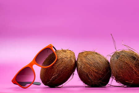 three whole coconuts and orange glasses on a pink background.の写真素材