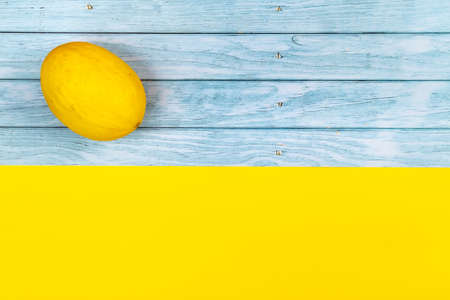 A whole yellow melon lies on a blue wooden background and a yellow background.の写真素材