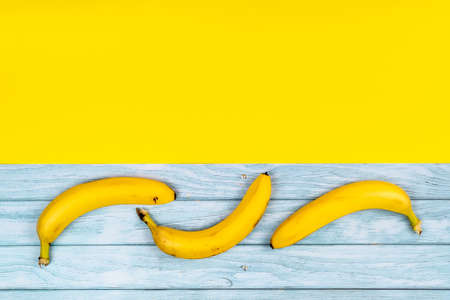 Yellow bananas lie on a blue wooden background and a yellow background.