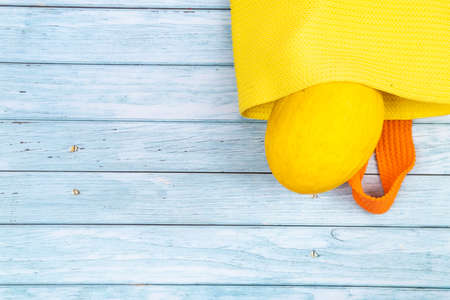 Oval melon lying in a yellow bag on a blue wooden background.