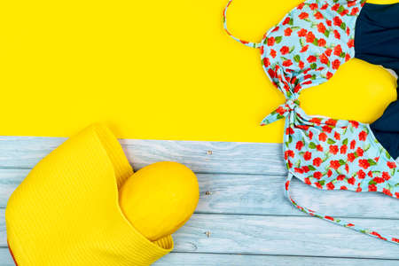 Top view of a swimsuit and a melon in a bag, lying on a blue wooden and yellow background.Summer vacation concept.の写真素材