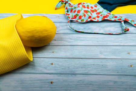 Top view of a swimsuit and a melon in a bag, lying on a blue wooden and yellow background.Summer...